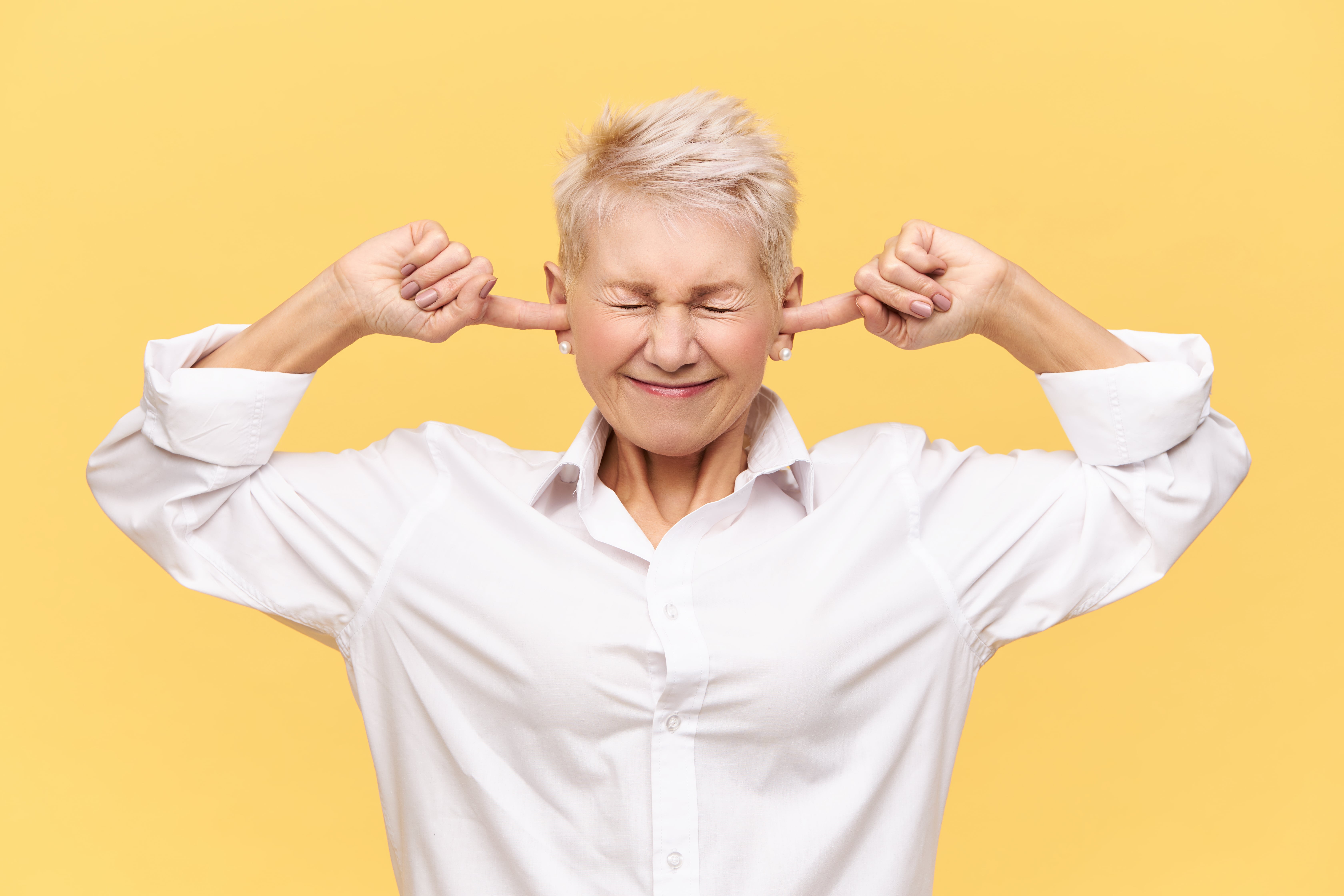 shut up isolated image of frustrated angry mature female with dyed pixie hair keeping eyes closed and plugging ears can t stand loud sounds or noise being stressed while having fight or argument min