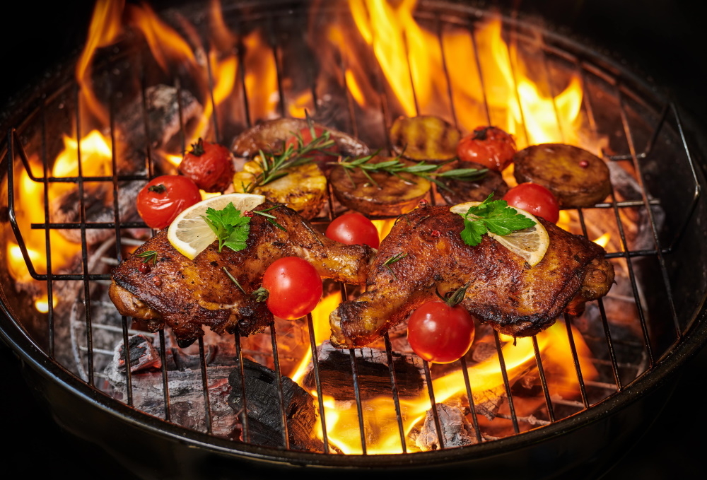 grilled chicken legs on the flaming grill with grilled vegetables with tomatoes potatoes pepper seeds salt